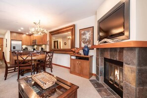 A modern kitchen with wooden cabinets, a dining area with a table and chairs, a fireplace, and a large mirror above the counter. - Free parking | Hot tub | Steps to Blackcomb (Whistler)