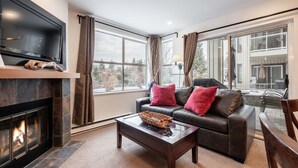 A living room with a fireplace, a leather sofa with red cushions, a coffee table, and a television mounted on the wall. - Free parking | Hot tub | Steps to Blackcomb (Whistler)