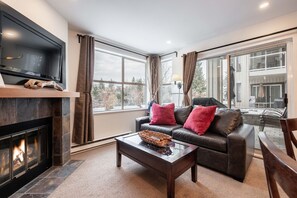 A living room with a fireplace, a leather sofa with red cushions, a coffee table, and a television mounted on the wall. - Free parking | Hot tub | Steps to Blackcomb (Whistler)