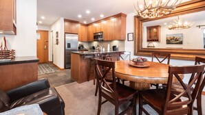 A modern kitchen with wooden cabinets, a stainless steel refrigerator, and a dining area with a wooden table and chairs. - Free parking | Hot tub | Steps to Blackcomb (Whistler)