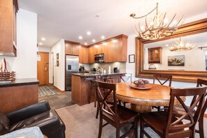 A modern kitchen with wooden cabinets, a stainless steel refrigerator, and a dining area with a wooden table and chairs. - Free parking | Hot tub | Steps to Blackcomb (Whistler)