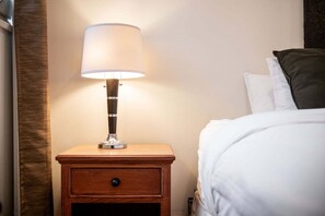 Et natbord i træ med en lampe, en skuffe samt en seng med hvidt sengetøj og en mørk pude.