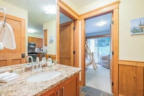 A bathroom with a marble sink, wooden cabinets, and a view of a deck through an open door. - Steps to Blackcomb | Free Parking | Hot tub (Whistler)