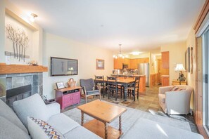 Een woonkamer met een open haard, een bank, een salontafel en een eethoek met stoelen en een tafel.