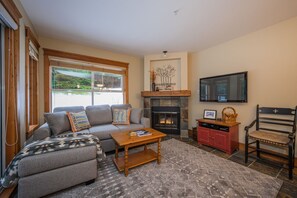 A living room with a fireplace, a sofa set, a coffee table, a TV, and a stone fireplace surround. - Steps to Blackcomb | Free Parking | Hot tub (Whistler)