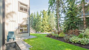 Ein Wohnhaus mit gepflegtem Rasen, einer Holzdiele und verschiedenen Bäumen und Sträuchern.