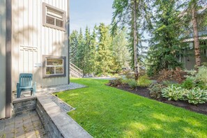 A residential property with a well-maintained lawn, a wooden deck, and a variety of trees and shrubs. - Steps to Blackcomb | Free Parking | Hot tub (Whistler)