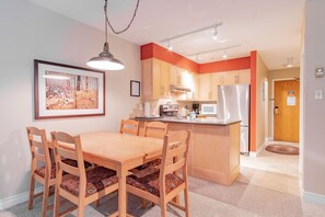 A compact kitchen with wooden cabinets, a stainless steel refrigerator, a dining table with four chairs, and a pendant light. - Hot tub | Steps to Blackcomb | Free parking (Whistler)
