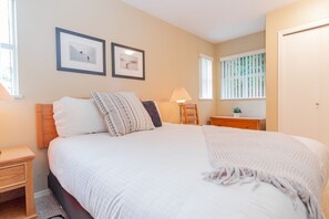 Een slaapkamer met een bed, nachtkastjes, een dressoir, een lamp en twee foto's in lijsten aan de muur.