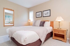A bedroom with a bed, two bedside lamps, a nightstand, a mirror, and two framed pictures on the wall. - Hot tub | Steps to Blackcomb | Free parking (Whistler)
