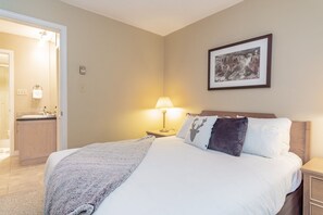 Een hotelkamer met een bed, een nachtkastje met een lamp, een ingelijst schilderij aan de muur en een badkamer door een geopende deur zichtbaar.