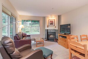 A living room with a fireplace, a television, a sofa, a coffee table, and a dining area. - Hot tub | Steps to Blackcomb | Free parking (Whistler)