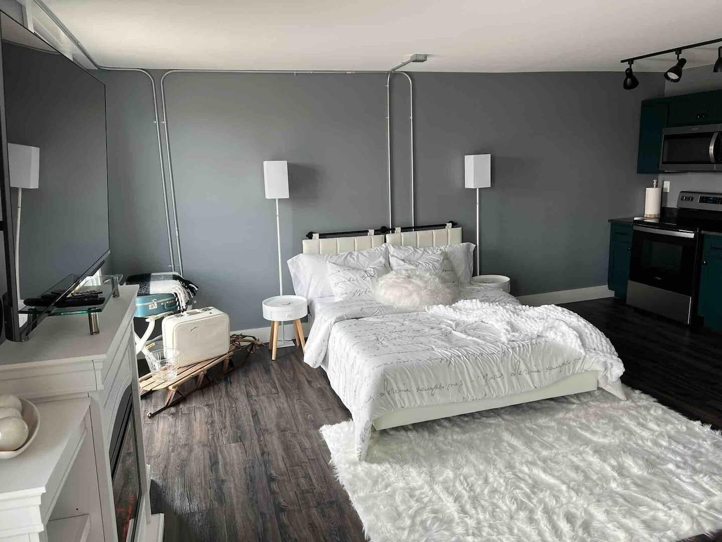 A modern bedroom with a bed, bedside tables, a dresser, a TV, and a kitchenette.