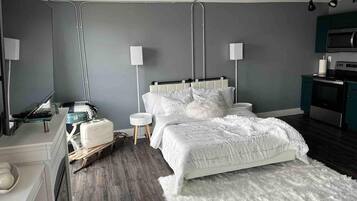 A modern bedroom with a bed, bedside tables, a dresser, a TV, and a kitchenette.