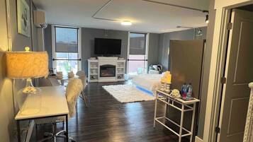 A modern living room with a fireplace, a dining area, and a hallway leading to a door.