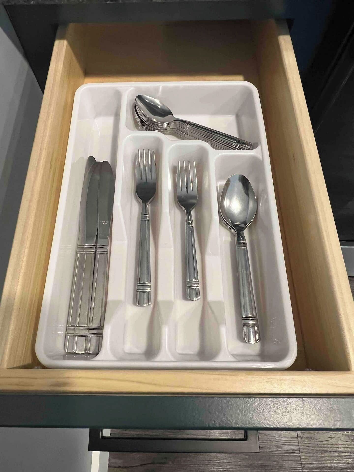 A drawer with compartments containing a knife, fork, spoon, and a set of chopsticks.