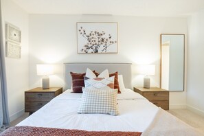 A neatly arranged bedroom with a bed, two bedside tables, a nightstand, a mirror, and a wall-mounted picture. - Bright condo | Close to Blackcomb | Free parking (Whistler)