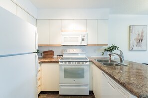 A compact kitchen with white cabinetry, a built-in microwave, a stove, and a granite countertop. - Bright condo | Close to Blackcomb | Free parking (Whistler)