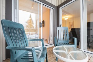 Un balcon avec deux chaises et une table, de grandes portes vitrées et une vue sur un arbre à l’extérieur.