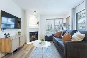 Un salon moderne avec une cheminée, un téléviseur à écran plat, un canapé avec des coussins et une table basse.