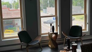 A room with three large arched windows, two chairs, a wooden table, and a view of a parking lot. - African Inspired 1BR Flat - Downtown Bellefontaine (Bellefontaine)