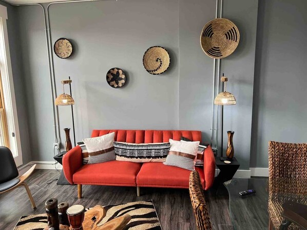 Una sala de estar moderna con un sofá rojo, platos decorativos tejidos y dos lámparas de pie.