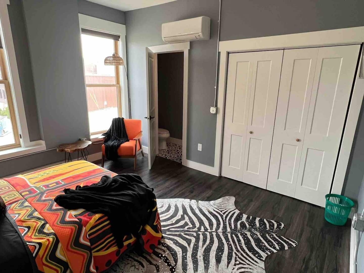 Een slaapkamer met een bed, een stoel, een tapijt met zebraprint, een kast en een raam.