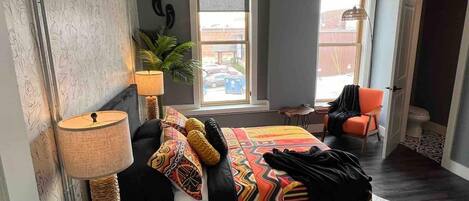 Un dormitorio con cama, dos lámparas, una ventana, una silla y una puerta.