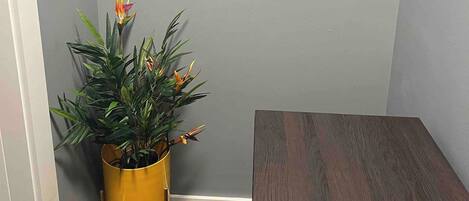 Rincón de una habitación con una pared gris, una mesa de madera y una maceta amarilla con plantas y flores verdes.