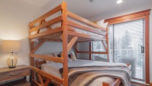 Un letto a castello con struttura in legno, un comodino con una lampada e una finestra con persiane.