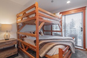 Ein Stockbett mit Holzrahmen, ein Nachttisch mit Lampe und ein Fenster mit Jalousien.