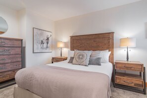 A bedroom with a large bed, two bedside tables, a wooden dresser, and a wall-mounted mirror. - Updated 2BDR | Perfectly located! Close to Gondola (Whistler)