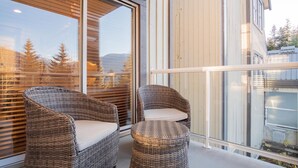 Un balcone con mobili in vimini e una porta vetrata che si apre su una vista di alberi e montagne.