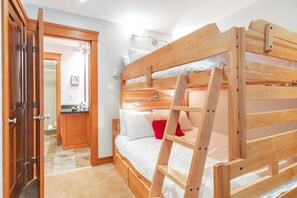 Ein Stockbett mit einer Leiter, eine Holztür und im Hintergrund ein Badezimmer.