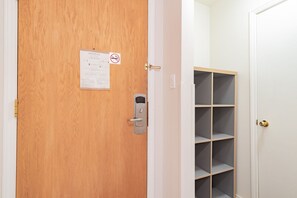 Una porta de fusta amb un teclat de seguretat, un cartell de prohibició de fumar i un avís sobre la sortida d'emergència.