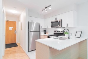 A modern kitchen with white cabinetry, stainless steel appliances, a built-in microwave, and a small island with a sink. - Stylish | Steps to Blackcomb | Free Parking (Whistler)