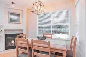 A dining area with a fireplace, wooden chairs, a table, and a window with blinds. - Stylish | Steps to Blackcomb | Free Parking (Whistler)