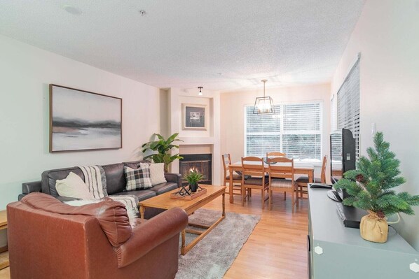 A living room with a sofa, coffee table, fireplace, dining table, chairs, and a small Christmas tree. - Stylish | Steps to Blackcomb | Free Parking (Whistler)