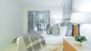 Um quarto com cama, luminárias de cabeceira, uma janela com persianas, um quadro na parede e uma pequena planta na mesa de cabeceira.