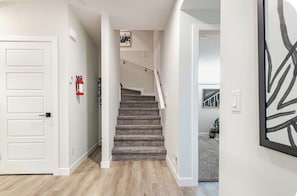 A staircase with a handrail, a white door, and a fire extinguisher on the wall. - Cozy & Stylish 1-Bedroom Suite Perfect for Couples or Solo Travellers (Calgary)