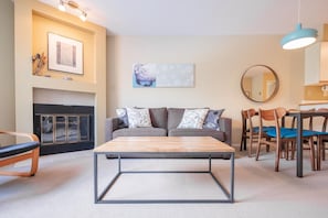 A living room with a sofa, coffee table, chairs, fireplace, and artwork on the walls. - Budget friendly Comfortable 1BDR | Close to Lifts (Whistler)