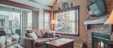 A cozy living room with a stone fireplace, leather sofa, and a television mounted on the wall.