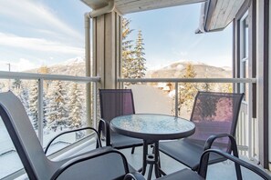 A balcony with a glass table and chairs, overlooking snow-covered trees and mountains. - Chic 2BDR + Loft | Perfect for Families or Friends (Whistler)