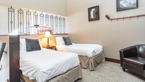 Hotellihuone, jossa on kaksi sänkyä, työpöytä, tuoli ja seinällä jääkiekkomaila.