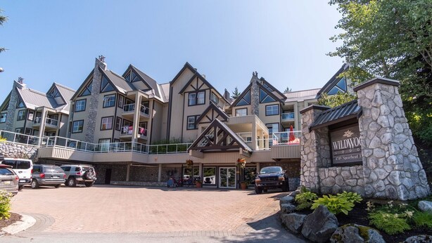 A multi-story lodge with a stone facade, balconies, and a parking area. - Modern 2BDR + Loft | Close to Ski Lifts and Shops (Whistler)