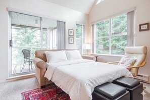 A bedroom with a large bed, a chair, a window, and a view of greenery outside. - Modern 2BDR + Loft | Close to Ski Lifts and Shops (Whistler)