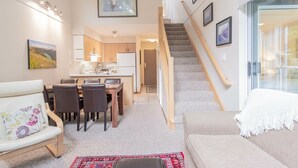 A modern interior with a dining area, kitchen, staircase, and seating space. - Modern 2BDR + Loft | Close to Ski Lifts and Shops (Whistler)