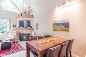 Una sala de estar moderna con chimenea, una mesa de comedor y un ventanal con vistas a la vegetación.