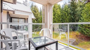 Ein Balkon mit Glasgeländern, weißen Plastikstühlen und einem Glastisch.