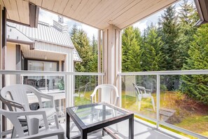 A balcony with glass railings, white plastic chairs, and a glass table. - Complex hot tub | Close to Lifts | Free Parking (Whistler)